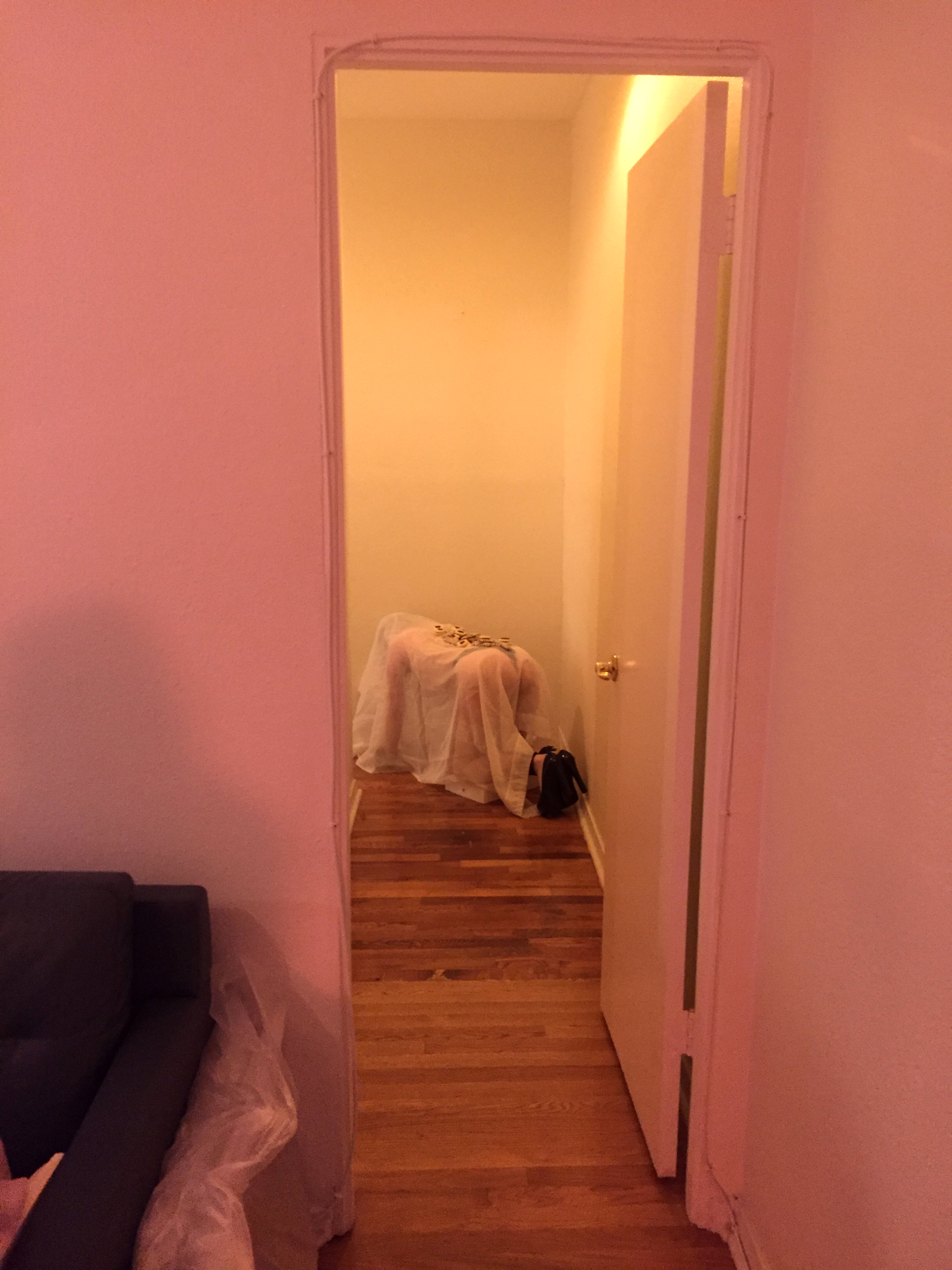 A girl on all fours with a sheer sheet over her in a narrow hallway in warm light